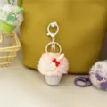 Detail view of a cute plush ice cream scoop keychain charm hanging on a yellow handbag. - White