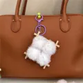 Close-up of fuzzy fermented bean curd keychain on a brown leather bag accessory. - Purple