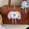 Detailed view of a cute curly-haired plush doll charm attached to a brown leather handbag. - Purple