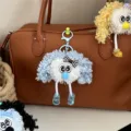 Detailed view of a cute blue curly plush doll keychain hanging on a brown leather bag. - Sky Blue