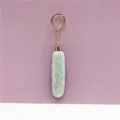 Close-up of mint green faux fur keychain with gold ring on mauve background - Green
