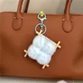 Detail view of a cute fuzzy pom-pom keychain attached to a brown leather handbag - Sky Blue