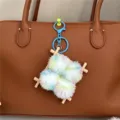 Close-up of a colorful fuzzy pom-pom bag charm with wooden frame on a brown leather bag. - Teal