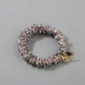 Detail of handmade grey crystal hair ring with a decorative gold-tone brand tag. - Gray