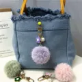 Close-up of a purple flower pom-pom keychain with a pearl charm hanging on a denim bag - 1 Piece / Lavender