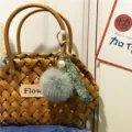 Detailed view of a floral strap keychain with grey pom-pom and pearl on a woven bag. - Single Piece / Green