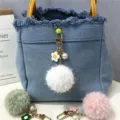 Close-up of cute white fur ball keychain with flower and pearl details on denim bag - 1 Piece / White