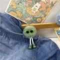 Close-up of cute green plush monster keychain with sunglasses on denim jacket - Green
