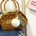 Detail view of a cute floral ribbon keychain with white fur pom-pom on a woven basket bag - Single Piece / White