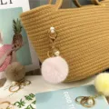 Detailed view of a soft pink plush pom-pom keychain with pearl charm on a woven straw bag - Pink