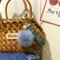 Close-up of a blue faux fur pom-pom and floral ribbon keychain hanging on a woven bag - Single Piece / Haze Blue