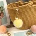Macro view of a cute yellow pom-pom keychain with a white pearl on a woven straw bag. - Goose Yellow