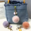 Close-up of fluffy floral pompom keychains and pearl charms on denim bag background - 1 Piece / Pink