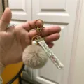 Close-up of elegant tweed ribbon keychain with beige plush pom pom and pearl - Khaki