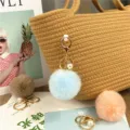 Close-up of pastel faux fur pom-pom keychain with pearl on a woven bag - Sky Blue