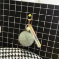 Detail of a green pom-pom keychain featuring a colorful ribbon and pearl accent - Green