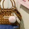 Detailed view of pink plush pompom keychain with floral ribbon and elegant pearl charm - Single Piece / Pink