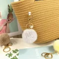 Detailed view of a soft grey pom-pom keychain with pearl accent on a woven bag. - Gray