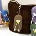 Macro view of colorful plush mustache keychains as cute charms on a brown leather bag. - Khaki