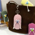 Close-up of cute pink plush keychain with mustache on a brown tote bag. - Pink