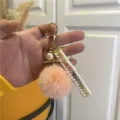 Close-up of elegant pink pom-pom keychain with gold hardware and pearl charm detail - Orange Pink