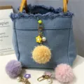 Detail view of colorful pom-pom charms with flower and pearl accents on denim bag - 1 Piece / Yellow