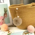 Close-up detail of a soft fluffy faux fur pom-pom keychain with elegant pearl charm. - Khaki