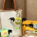 Cute plush monster keychain with black bat wings hanging on a white textured handbag - Single OPP Bag Packaging / Avocado Green
