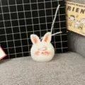 Close-up of a white fluffy bunny plush keychain with pink cheeks and a hair clip accessory. - Single OPP Bag Packaging / Orange Pink