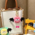 Detail view of a cute pink plush monster keychain with black bat wings on a white bag. - Single OPP Bag Packaging / Rose Red