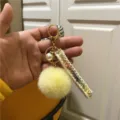 Close-up of yellow pom-pom keychain with tweed strap and pearl decoration - Goose Yellow