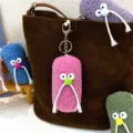 Close-up detail of a cute pink plush mustache monster keychain hanging on a brown bag - Rose Red