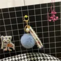 Detailed view of a light blue pom-pom keychain with tweed ribbon and pearl charm - Haze Blue