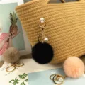Macro detail of a soft black plush pom-pom keychain with elegant pearl on a straw bag - Black