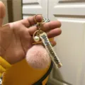 Macro view of pink plush pom-pom keychain featuring an elegant pearl and tweed ribbon charm - Dusky Pink