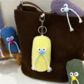 Detail view of quirky plush mustache character keychain charm on a brown leather bag - Yellow