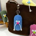 Close-up of quirky blue plush mustache keychain hanging on a stylish brown suede bag - Blue