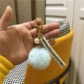 Close-up detail of a tweed style keychain featuring a blue faux fur pom pom and pearl - Sky Blue