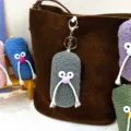 Cute gray plush mustache man keychain charm hanging on a stylish brown suede tote bag. - Gray
