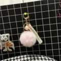 Close-up of a pink fluffy pompom keychain featuring a pearl charm and elegant woven ribbon. - Pink