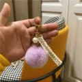 Detail of a purple faux fur pom-pom keychain with pearl charm and gold lobster clasp - Purple