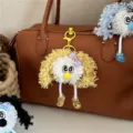 Detail shot of a curly yellow plush monster keychain hanging on a brown leather bag. - Yellow