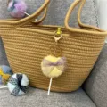 Close-up of a cute yellow plush lollipop keychain with a purple bow on a brown woven bag. - 1 Piece / Goose Yellow