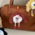 Detailed view of a cute curly-haired plush doll keychain hanging on a leather bag - Brick Red