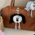 Detailed view of a cute curly-haired fuzzy doll keychain hanging on a brown leather bag - Black