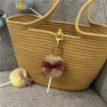 Detail view of a cute plush lollipop keychain with maroon lace bow on a woven bag - 1 Piece / Khaki