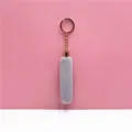 Close-up detail of a soft gray plush tassel keychain with a polished golden metal ring. - Gray