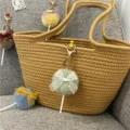 Detailed view of a cute plush lollipop keychain with a lace bow hanging on a woven bag. - 1 Piece / Dark Green