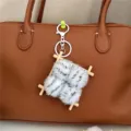 Close-up of cute plush fermented bean curd keychain attached to a brown leather bag. - Gray