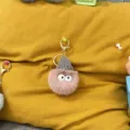 Close-up of a cute fuzzy pink plush keychain with a grey knit hat on yellow fabric. - 1 Piece / Dusky Pink